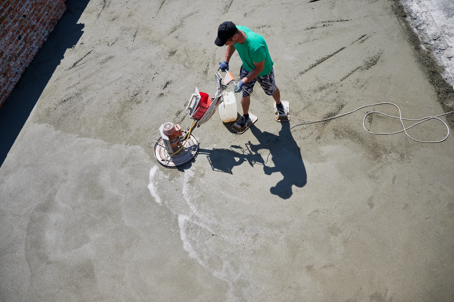 A person operating a concrete float on a freshly poured concrete surface.