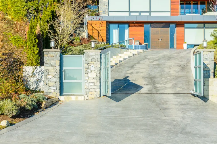 A modern house entrance with a concrete driveway, stone walls, and large glass doors.